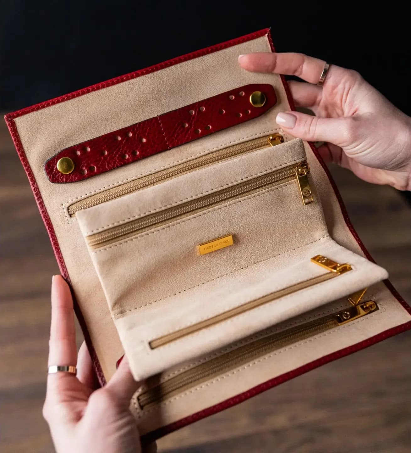 Hands opening the burgundy Viaggio Roll, suede lining, zipped pockets and a snap strap.